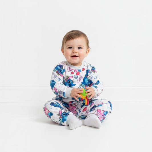 Twinkles baby wearing a white thermal pajama set with Stitch and Angel print, sitting on a white floor.