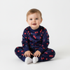 Baby wearing a Twinkles navy blue velvet pajama set with a red cherry print, sitting on a white background.