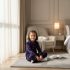 A young girl wearing a Twinkles navy blue cherry-print fleece pajama set, sitting on a rug in a cozy bedroom.