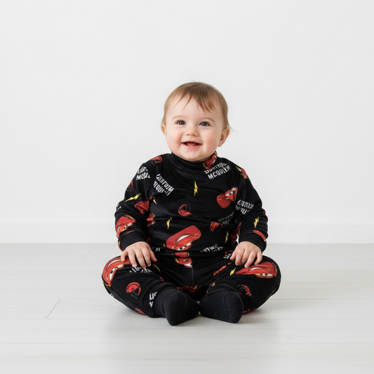 Twinkles baby wearing a black fleece pajama set featuring Lightning McQueen car prints and yellow lightning bolts