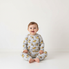 Twinkles baby wearing a grey long-sleeve Simba print pajama set while sitting on a white floor