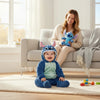 Twinkles baby wearing a blue fleece Stitch character jumpsuit with a hood, sitting on a rug near a smiling mother.